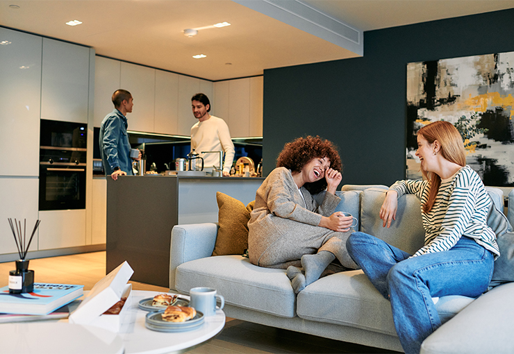 Two women chatting on the sofa and two men talking in an open plan kitchen