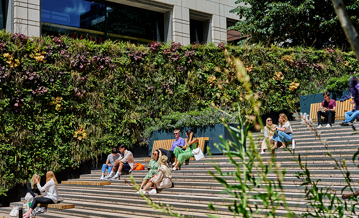 People sitting on the steps next a living wall at Canary Wharf